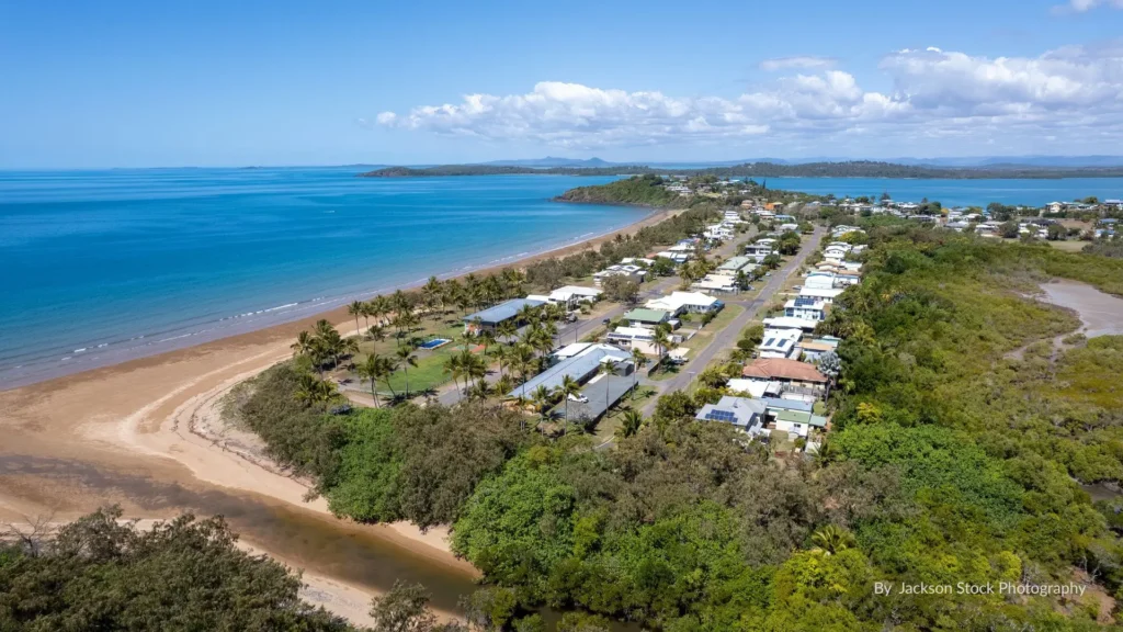 Aerial view of Sarina Beach showing wide sandy shoreline, calm blue Coral Sea, foreshore park and houses on the peninsula south of Mackay, Queensland.