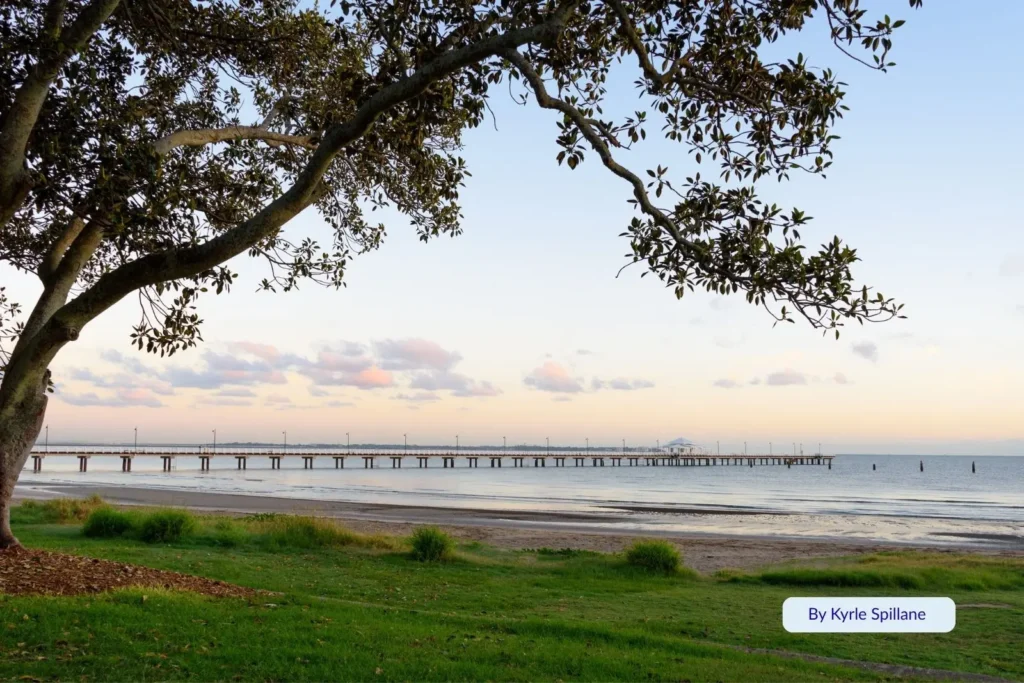 View of Sandgate Pier framed by trees at low tide on the foreshore in Brisbaneβs bayside.